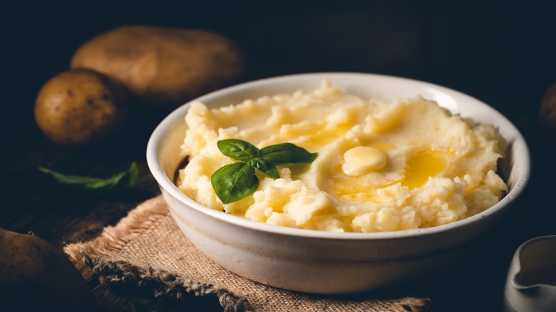 White bowl of mashed potatoes on wooden board