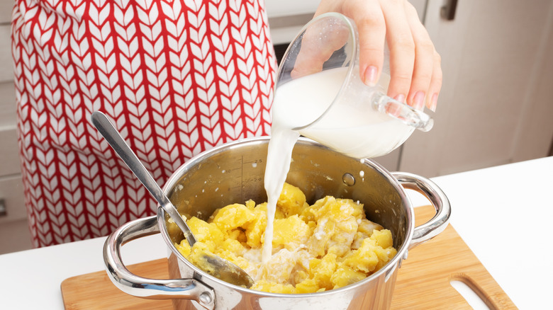 Hand adding milk to pot of mashed potatoes