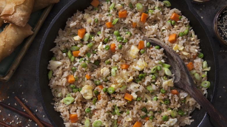 fried rice in a wok with a wooden spoon and a plate of spring rolls