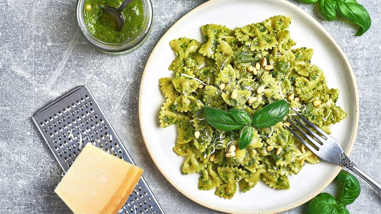 Plate of bow-tie pasta with pesto sauce, pine nuts, and shaved parmesan cheese