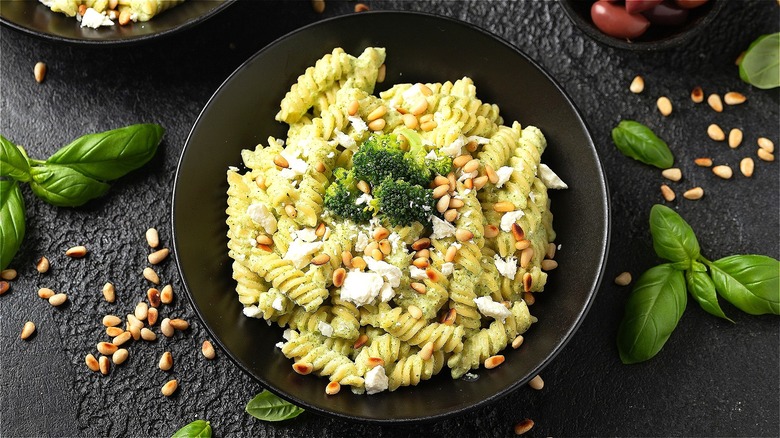 Bowl of fusilli pasta mixed with a pesto cream sauce and topped with feta cheese, pine nuts, and broccoli