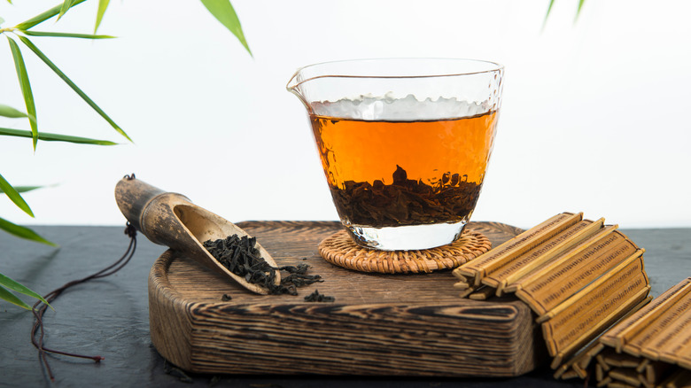 Brewed black tea in a clear glass with a wooden scooper filled with loose tea
