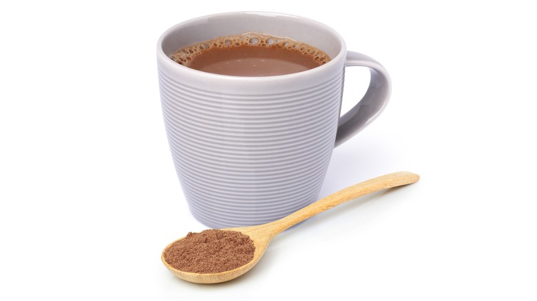 A spoon with malted milk powder next to a cup