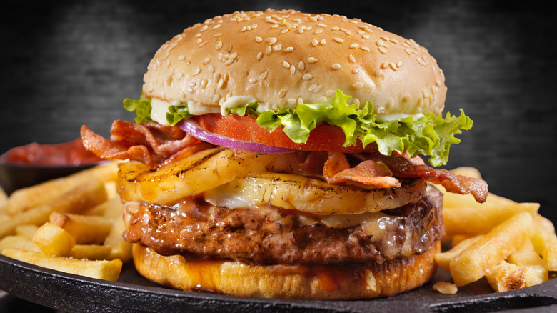 Burger on a sesame seed bun on a plate with fries.