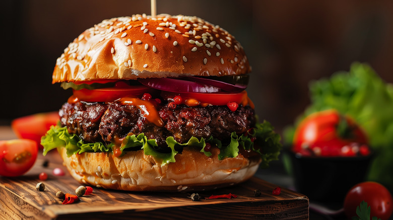 Hamburger on sesame seed bun sitting on a wooden board.