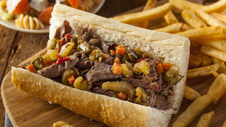 Italian beef sandwich with a side of French fries on a wooden tray with pasta salad in the background