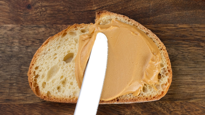 a shiny knife smears peanut butter on airy bread