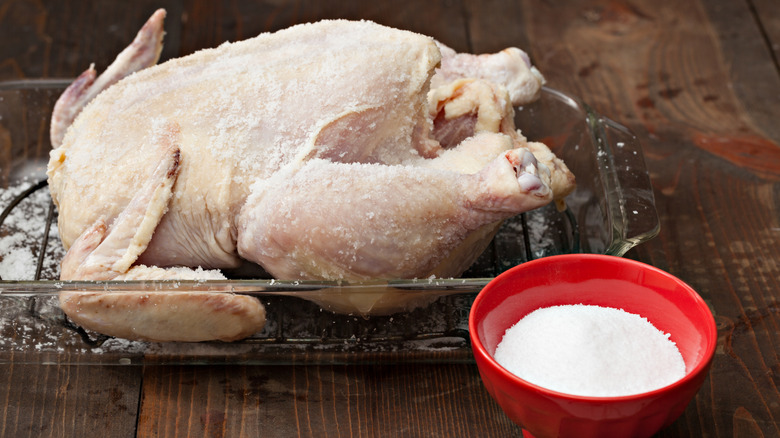 A whole chicken with a salt brine in a glass baking tray