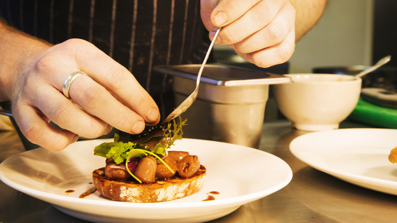 Hands of a chef plating food.