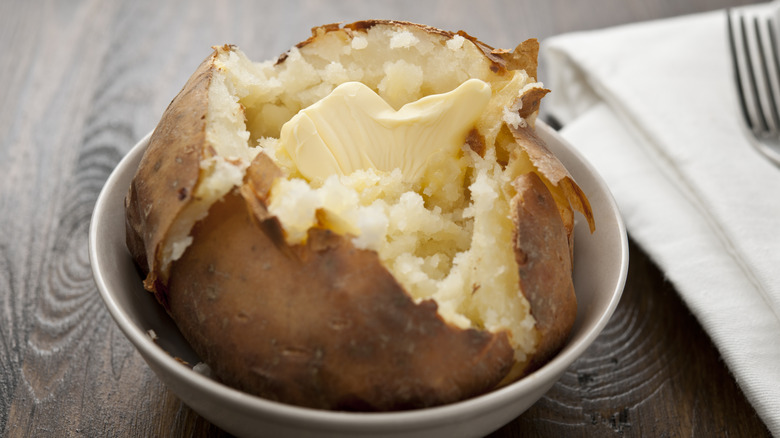 A cut-open baked potato with melting butter in a bowl