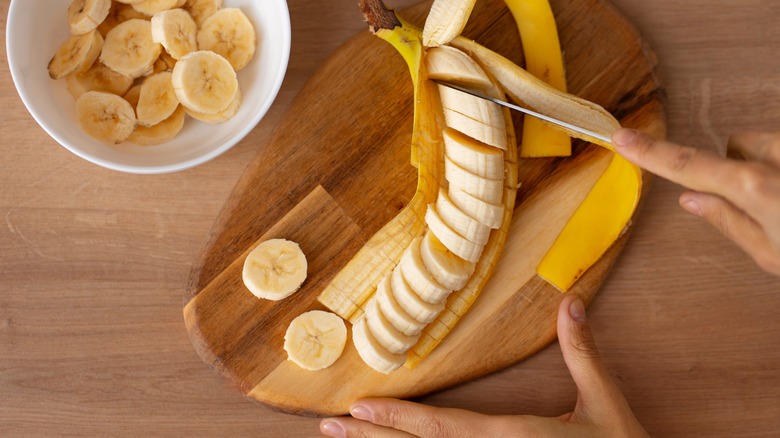 Hand slicing banana on cutting board