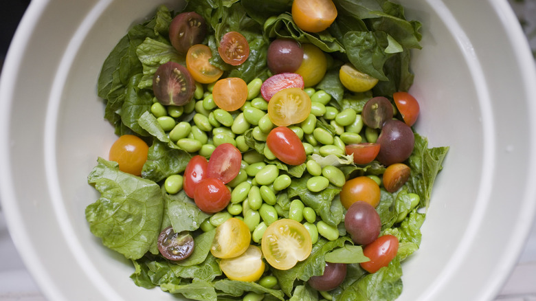 Lima beans mixed with salad greens and rainbow cherry tomatoes in a white bowl