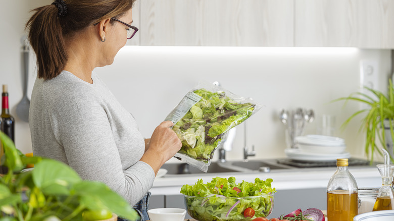 Woman reads label on a bag of prepackaged salad in kitchen