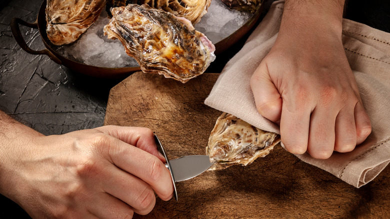 hands shucking oyster with knife
