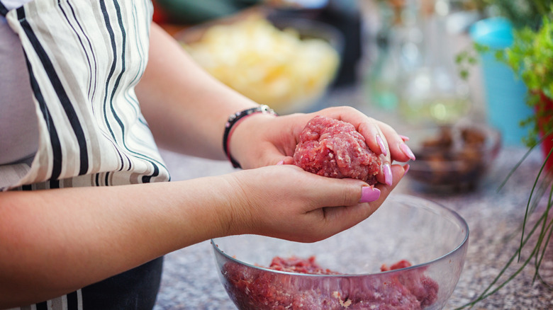 A woman's hands form raw ground beef into a patty