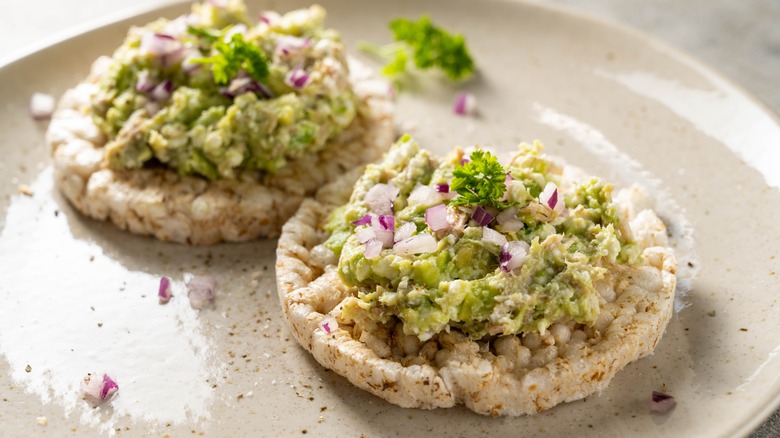 Two rice cakes topped with avocado tuna salad, red onion and parsley