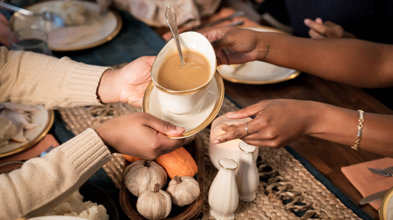 One person passing gravy boat to another person across a table