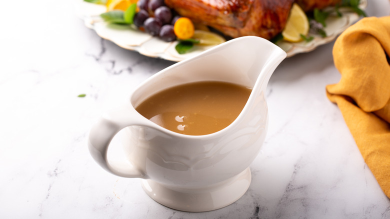 Gravy in a white gravy boat on marble surface next to roast chicken