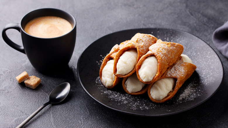 Italian cannoli with ricotta cheese on black plate with cup of coffee