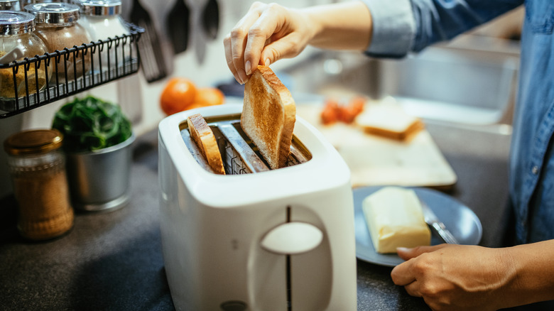 Hands taking bread out of toaster in kitchen