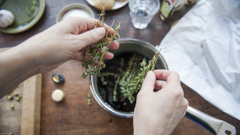 Person adding fresh thyme sprigs to a steel pot