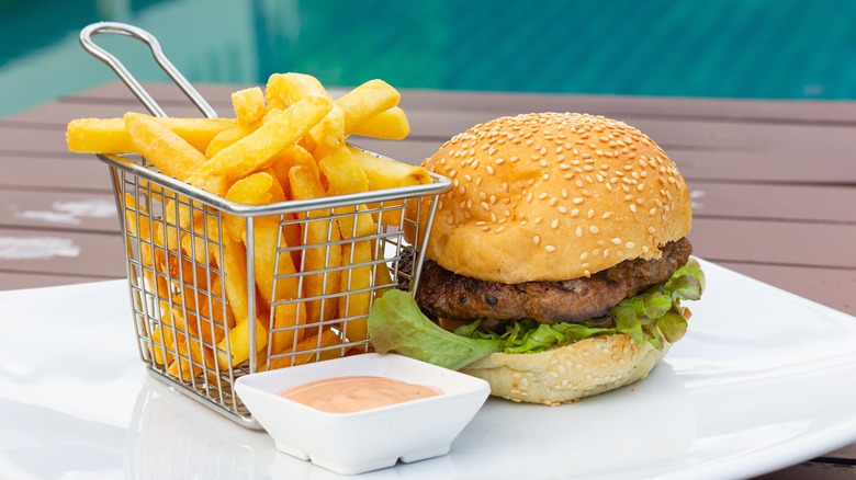 Hamburger and metal basket of french fries next to small white dish of fry sauce