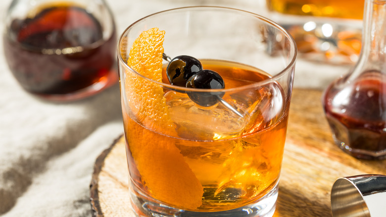 Brownish-orange cocktail in a rocks glass with an orange peel and two cherries