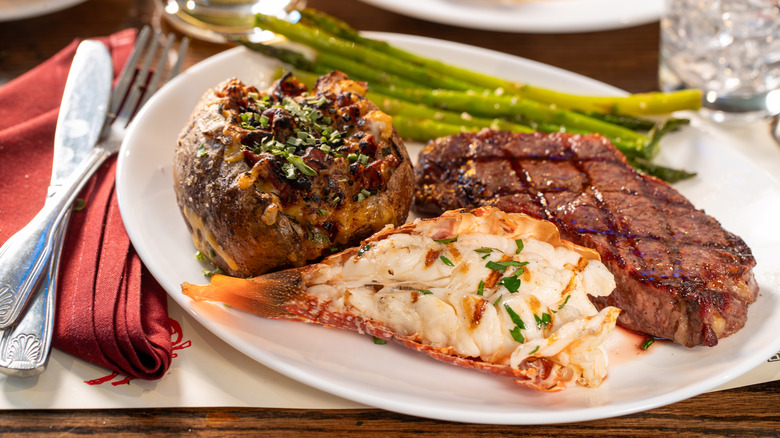 A steak and lobster tail entree at LongHorn Steakhouse, with asparagus and a loaded baked potato also on the plate