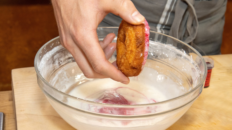 a person dipping a donut into glaze