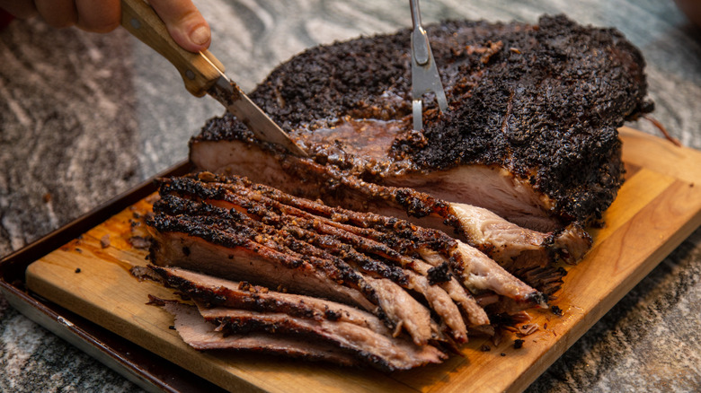 a person slicing a brisket on a wooden cutting board