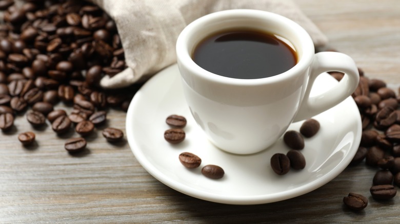 A white mug of coffee with coffee beans