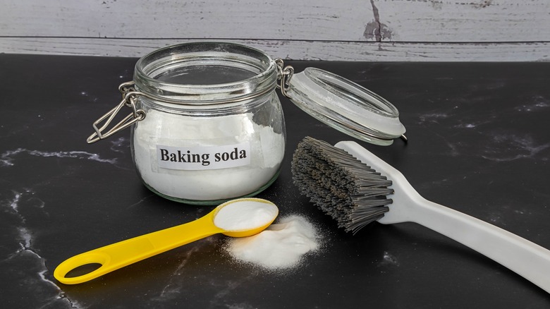 A jar of baking soda next to a spoon and a brush