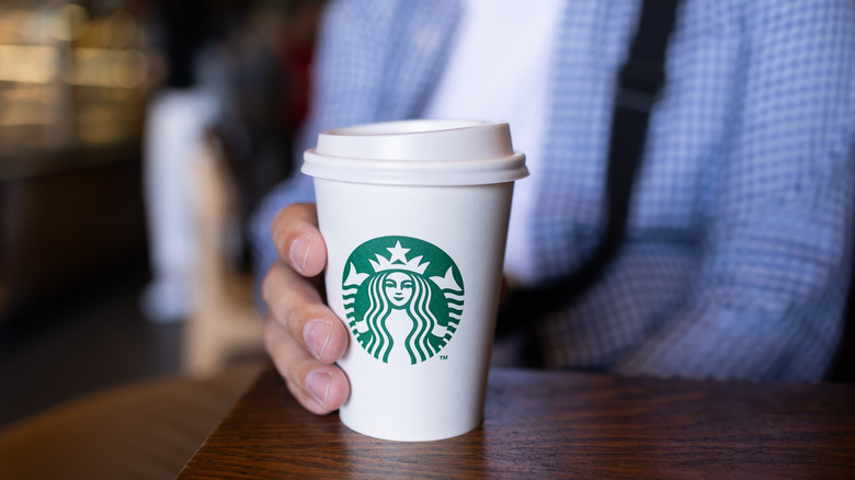 A Starbucks customer holds a small cup of hot coffee on a dark wood table