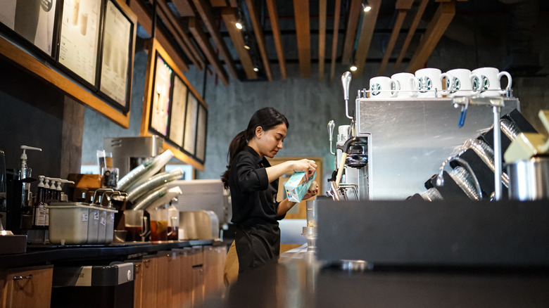 A Starbucks barista pours steamed milk into a cup while preparing a drink