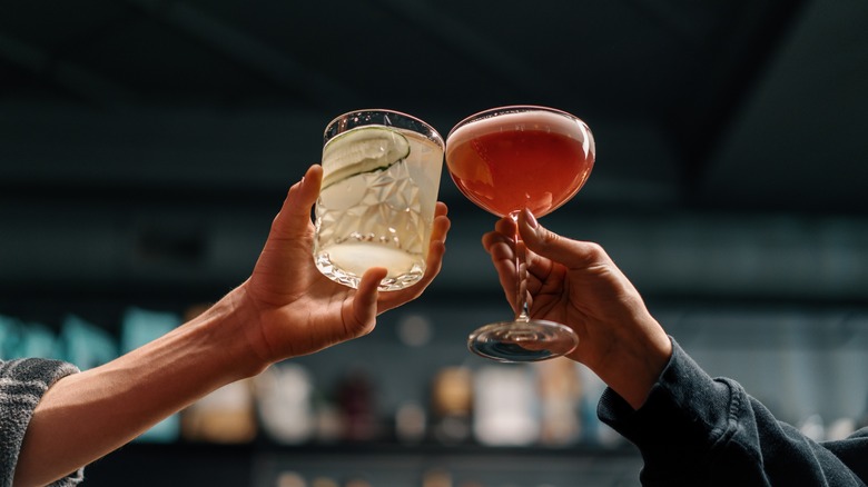 Two people holding mixed cocktails reach out to click glasses