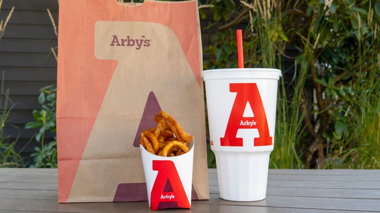 Arby's bag next to glass of cola and curly fries