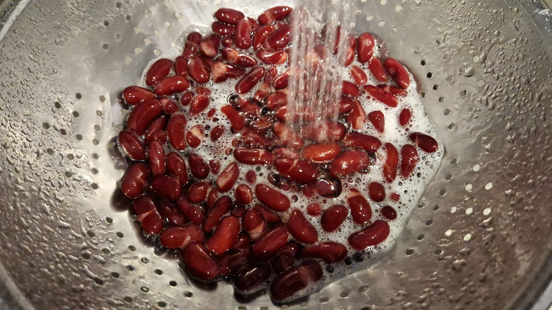 Kidney beans being rinsed in a metal colander under a stream of running water