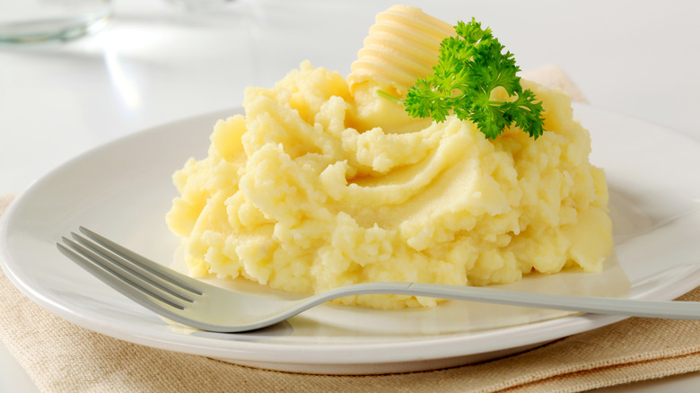 mashed potato with butter and parsley on plate with fork 