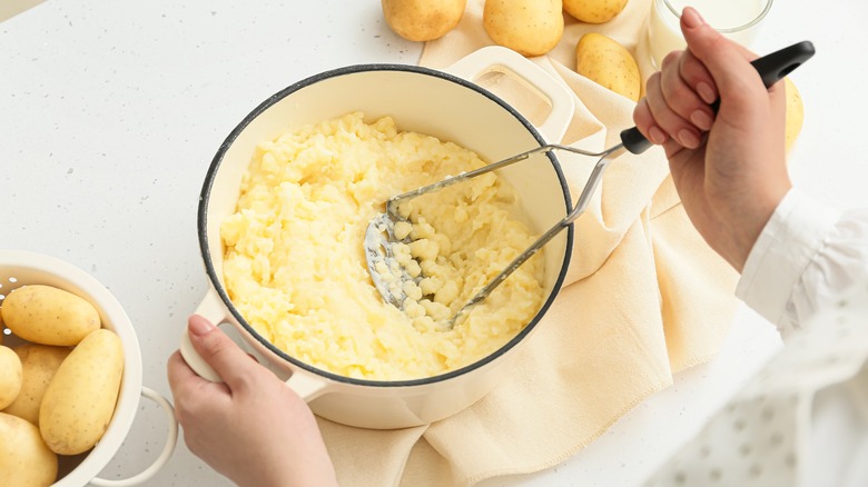 cook mashing potatoes in a white pot