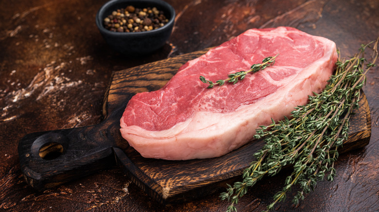 Raw New York strip steak garnished with herbs on wooden board