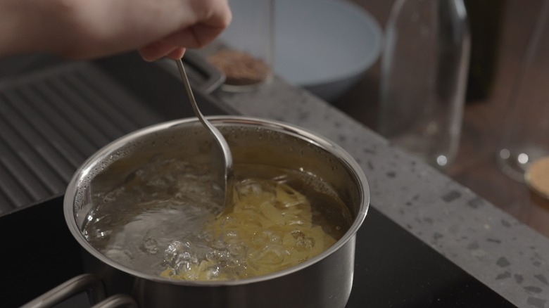 noodles cooking in boiling water being stirred with a metal spoon