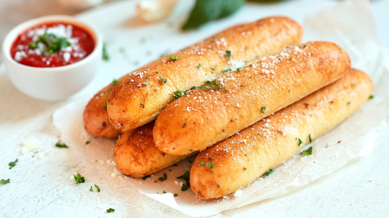 Pile of parmesan and herb covered breadsticks next to a small bowl of marinara sauce