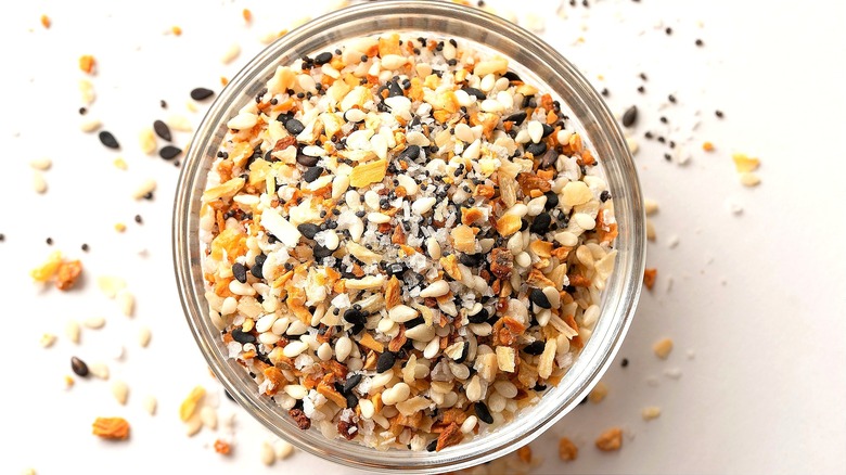 A clear bowl is overflowing with everything bagel seasoning on white background.