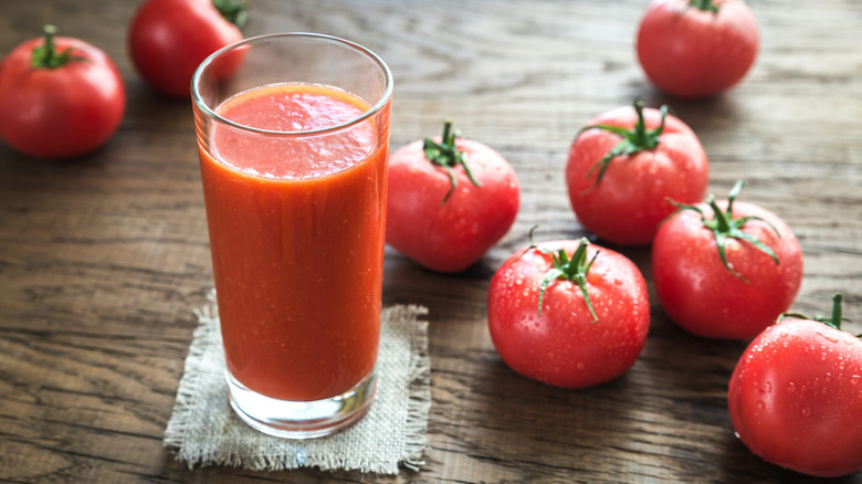 A glass of vegetable juice is surrounded by tomatoes.