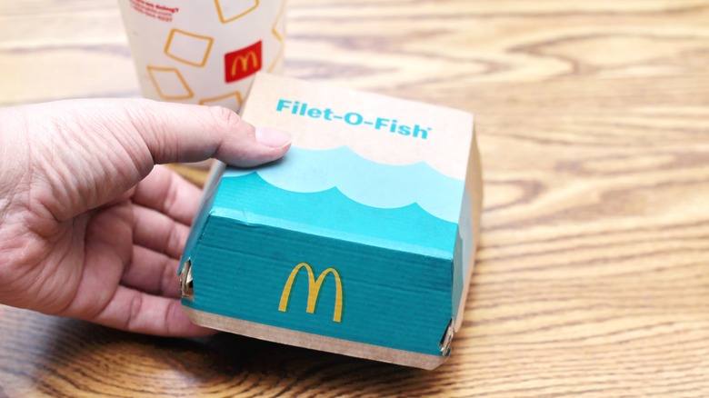 hand holding Filet O Fish box with drink cup in background