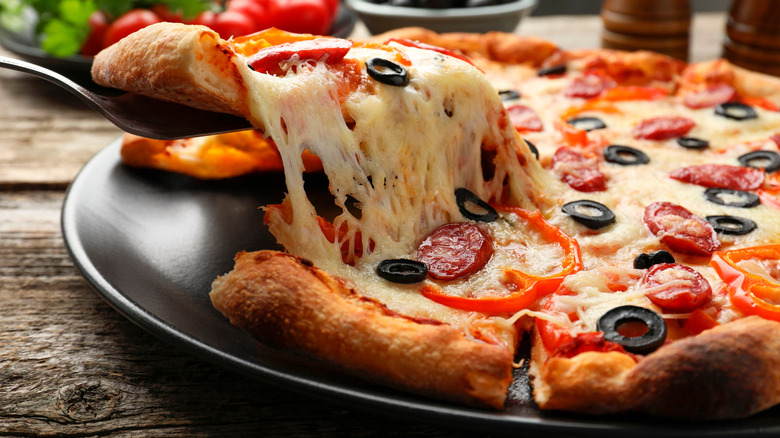 A slice of pizza is lifted off a pan with a serving utensil