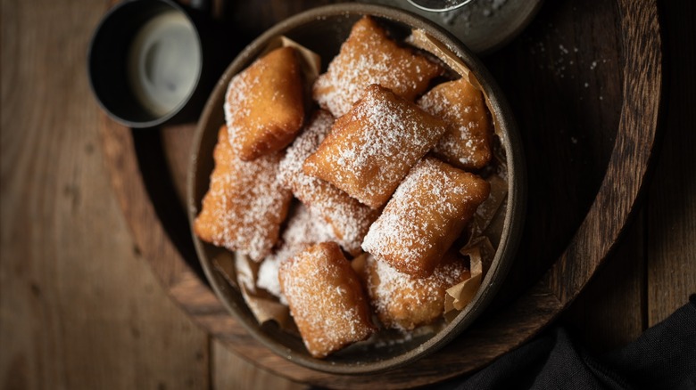 A bowl of fasnachts dusted with sugar on a wooden table