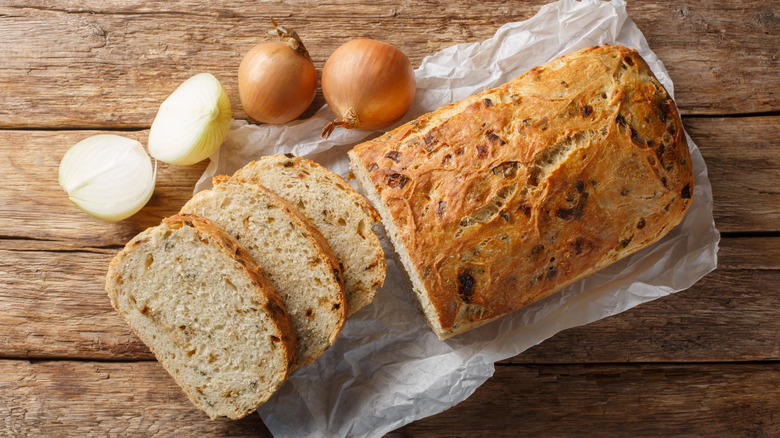 Loaf of onion bread on wooden board next to some fresh onions