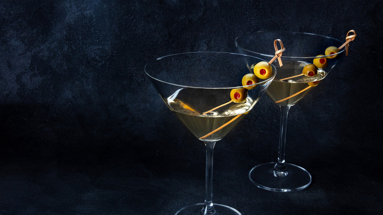 Two martinis with olives next to each other against a dark background