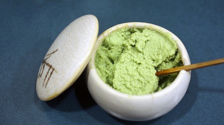 Green wasabi in a white bowl with Japanese writing on the lid and a chopstick in it